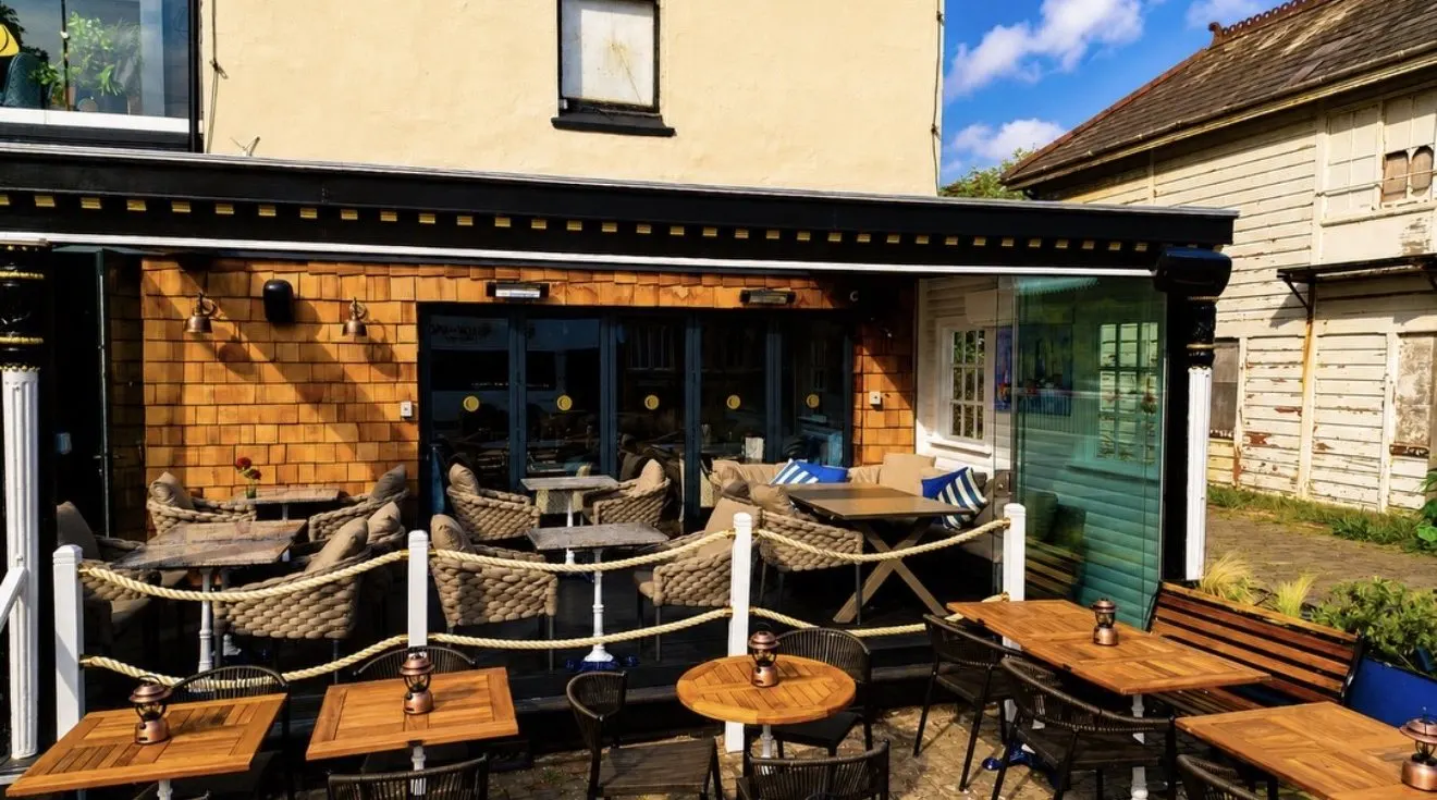 The sunny courtyard at Coast, with wooden tables in front of the covered terrace